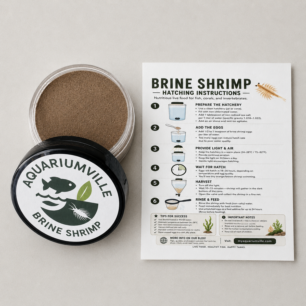Aquariumville Brine Shrimp eggs product shown with an open clear jar containing brownish-brown powder, a black lid with the Aquariumville logo, and an instruction sheet explaining how to hatch brine shrimp on a light neutral background.