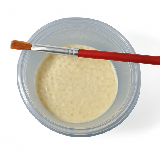 Microworm culture in a clear plastic cup with a small paintbrush resting across the top, used for feeding fry and starting new cultures.