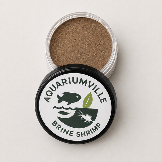 An open round plastic jar filled with brown brine shrimp eggs, shown with its black lid in front. The lid has a white label with the brand name 'AQUARIUMVILLE' and 'BRINE SHRIMP' in dark green text, along with a fish, shrimp, and leaf graphic.