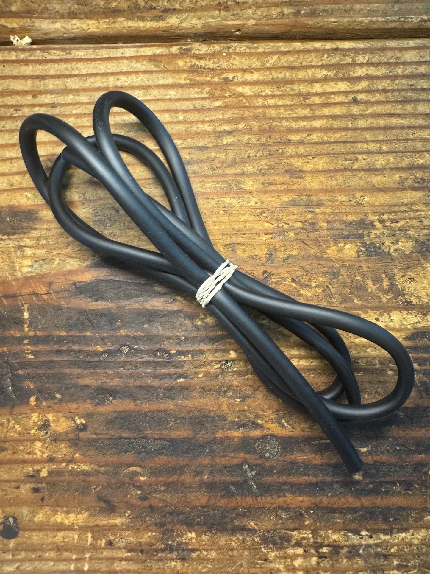 Black aquarium airline tubing coiled and secured with a twist tie, displayed on a rustic wooden surface — used for connecting air pumps, airstones, and filters in freshwater or saltwater aquariums.