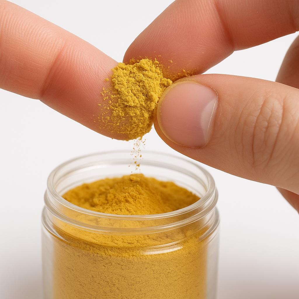 Close-up of fingers holding a small pinch of golden yellow bee pollen powder above an open jar.